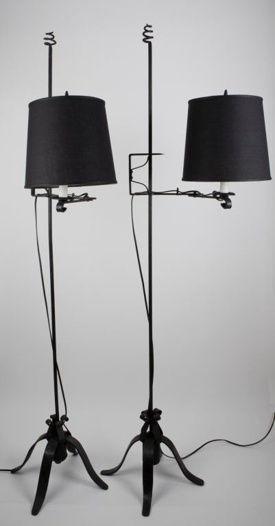 TF1770<br />
A pair of black wrought iron adjustable height bridge-arm floor lamps having counterweighted tripod bases and pig-tail finials with black fabric shades.<br />
<br />
Overall dimensions: 67