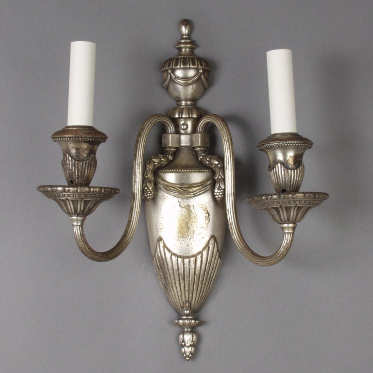 AIS1684
A pair of two arm sconces in their original worn silverplate over bronze finish. The backplates and cups are detailed with gadrooning, swags and beading. The reeded arms terminate in berried ferrules. Signed by the Connecticut maker Bradley