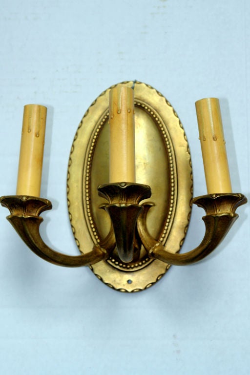 Pair of circa 1930s three-light sconces with gilt finish, oval backplate with beading and scalloped detail.

Measure: 10