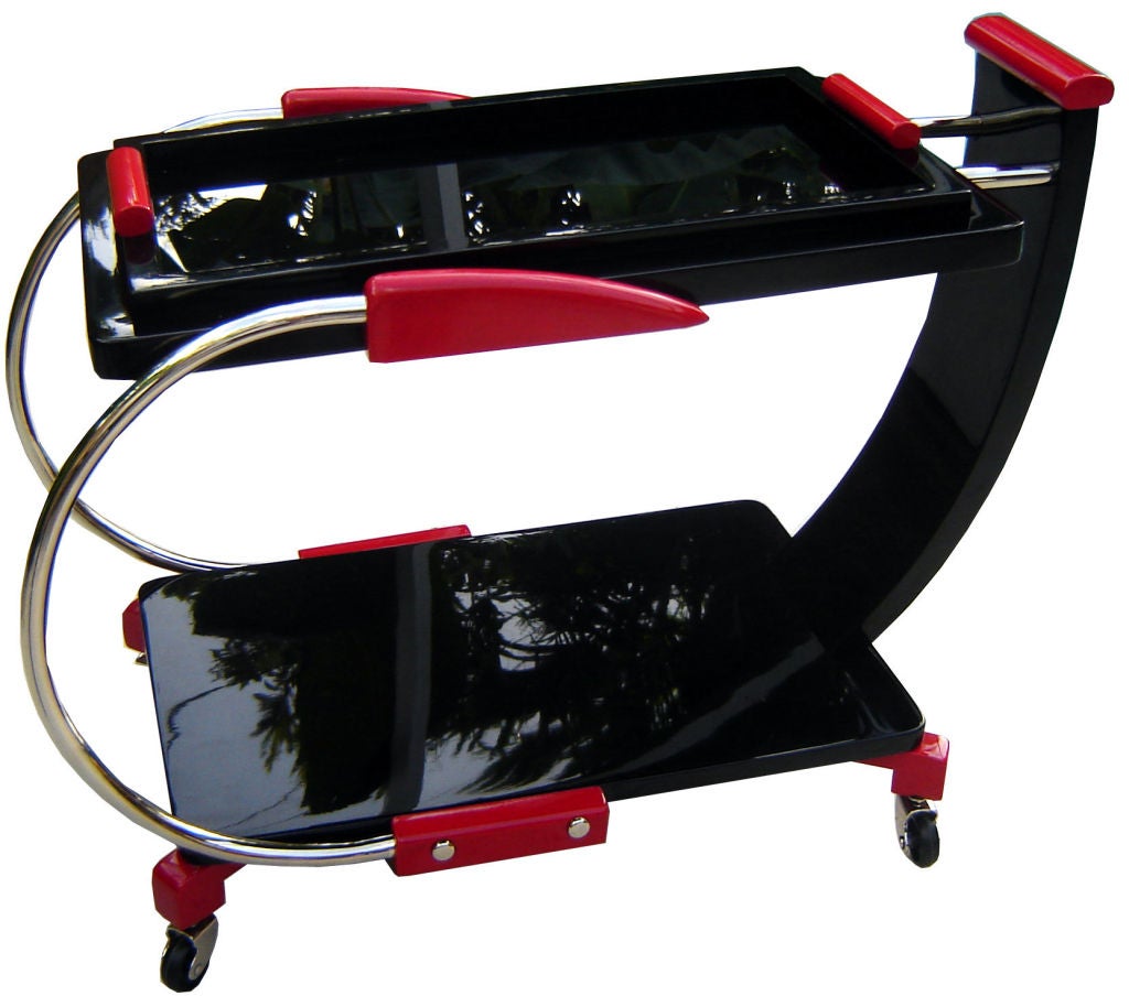 This ca. 1935 American art deco bar cart or tea trolley is sculpture on wheels!  Finished in black and red lacquer with nickel fittings, the cart seems to be moving while standing still.  The black glass tray on top with red handles removes for