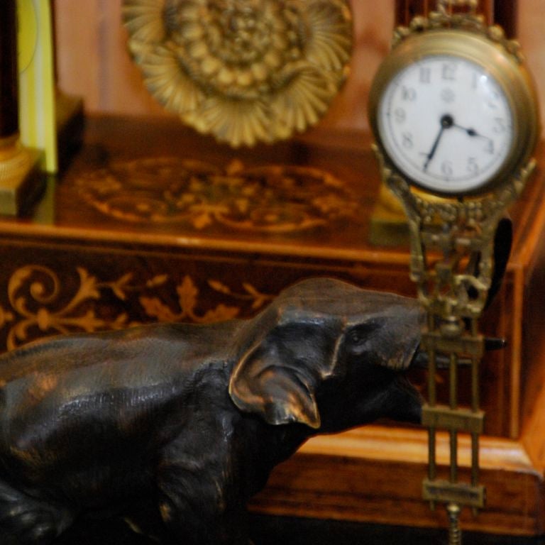 A bronzed elephant on oval wood base with upraised trunk holding the swinging clock mechanism