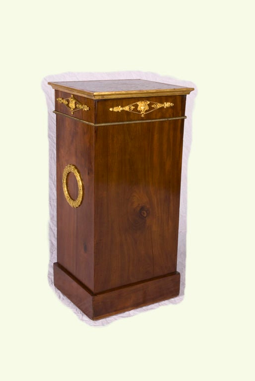 The clean, elegant lines of this cabinet from the early 19th century are accented by lovely gilt bronze and wood details.  A single cupboard door reveals a single interior shelf. Perfect as an end table or nightstand, the beautiful graining of the