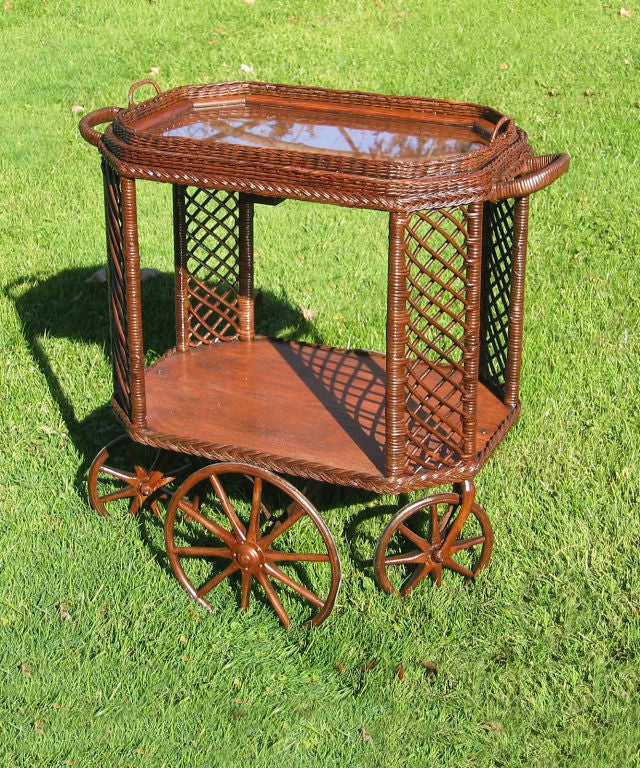 Bar Harbor style wicker tea cart having 4 wood-spoked wheels.  Hallmark Bar Harbor lattice design to 4 angled corner panels.  Two quarter sawn oak surfaces with wicker framed removable glass tray on top.  CORNER HOUSE ANTIQUES offers an extensive