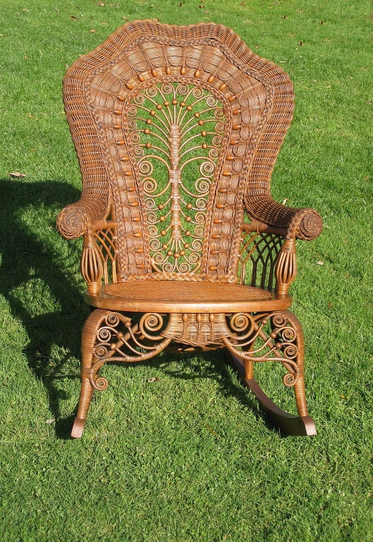 Ornate Victorian wicker rocker in original natural stained finish. Serpentine rolled crest and arms ending in fancy twist-wrapped rosettes. Multiple curlicues & wooden beadwork throughout. Cane-wrapped cabriole legs with elaborate front skirt.
