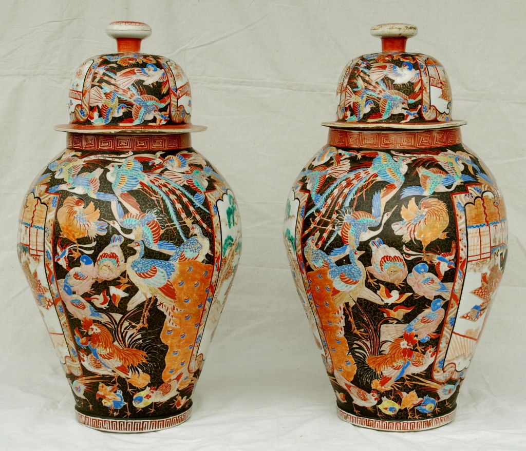 The covered baluster vases decorated in polychrome enamels and gilt over a clear glaze with panels of courtiers, the surrounding areas painted with various birds, the neck and foot banded by ket frets; chrysanthemum finial