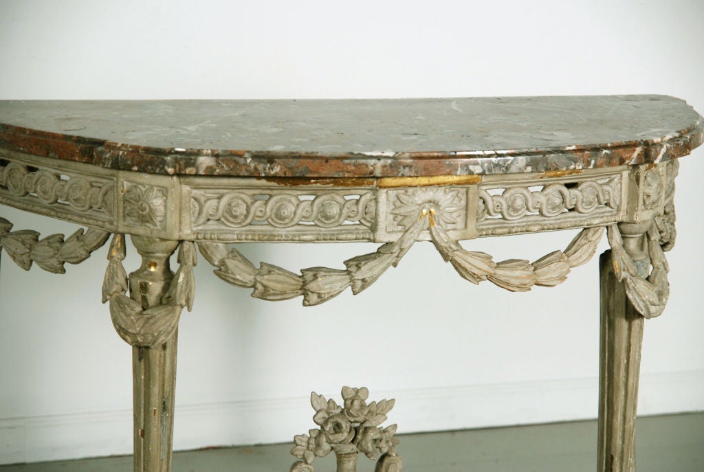 A Louis XVI Grey Painted Console<br />
Circa 1780<br />
Attributed to George Jacob <br />
<br />
Georges Jacob Maitre in 1765<br />
<br />
The demi-lune mottled marble top above a pierced foliate carved frieze, on tapering fluted legs headed