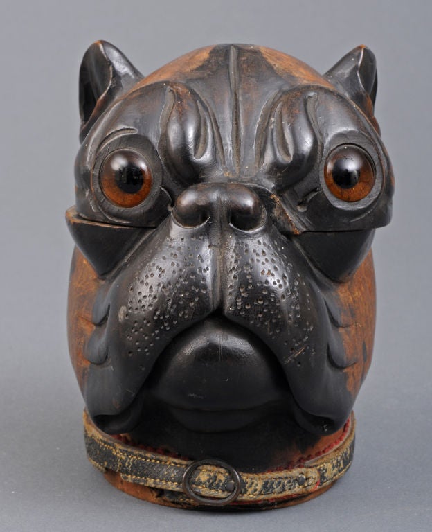 Lignum vitae inkwell modeled as the head of a bulldog with glass inset eyes and original leather collar. The head is hinged and opens to reveal brass top which is also hinged to reveal glass ink insert.