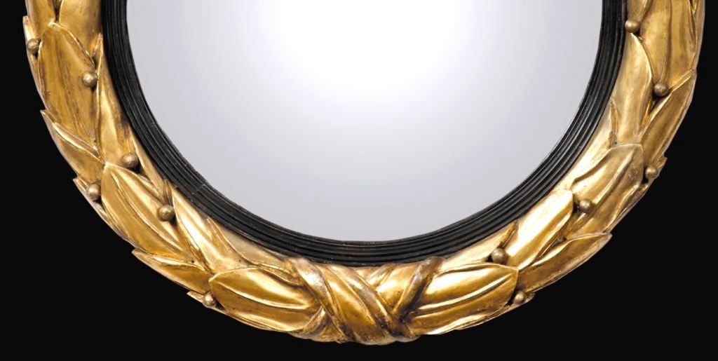 Unusual Regency giltwood convex mirror boldly carved with laurel leaves and berries tied with ribbon at the bottom, the convex mirror with ebonized reeded slip.