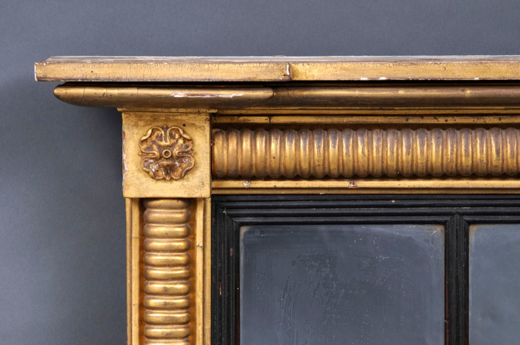 William IV giltwood overmantel mirror with three mirror plates surrounded by reeded moldings with carved Tudor roses mounted on corner blocks under the cornice, ebonized reeded slip. Paper label on back reads: Cole, Essex (England).