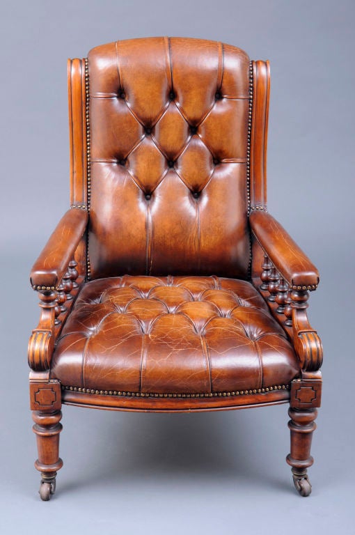 Victorian mahogany library armchair with turned, spindled and carved  arm supports, turned legs on brown porcelain casters, upholstered in brown buttoned leather with brass nail heads.
