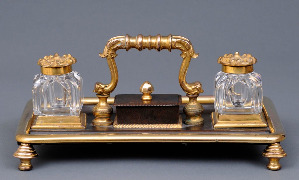 William IV gilded bronze inkstand with two molded glass inset inkwells with hinged bronze covers, stamp box with cover and finial, dolphin-shaped handle, raised on beehive-shaped feet.