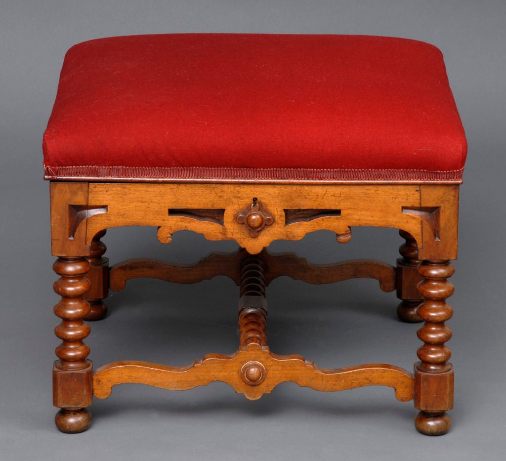 Victorian walnut ottoman/stool with hinged lift-top in the style of Richard Bridgens, carved open-work frieze and stretcher with bobbin-turned legs and cross-stretcher on bun feet.  Top upholstered in red wool felt.