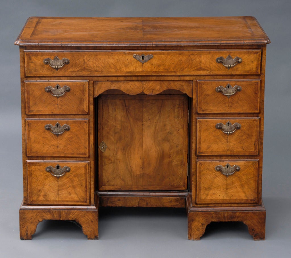 Victorian walnut veneered ladies kneehole desk with feathered banding around top and drawers, brass hardware, re-entrant corners, one long drawer over a shallow recessed cupboard with door, the interior revealing one shelf, flanked on either side by