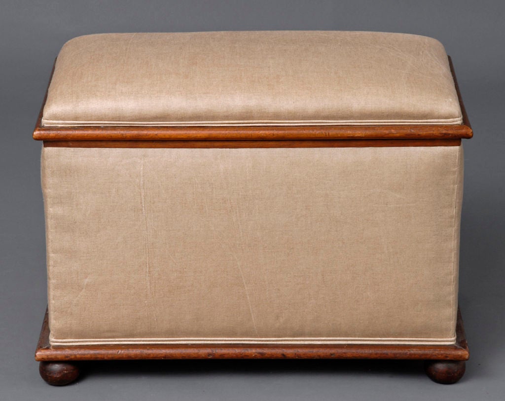 Mahogany ottoman with hinged lift-top, supported on ball feet. Upholstered in beige linen; inside lined in white cotton.