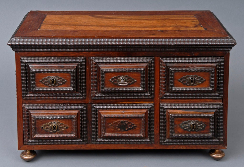 Miniature Portuguese rosewood chest with four drawers. Top, drawers and sides with carved moldings, brass pierced key escutcheons, resting on brass turnip-shaped feet. The drawers open in different sequences: the drawer on the right opens