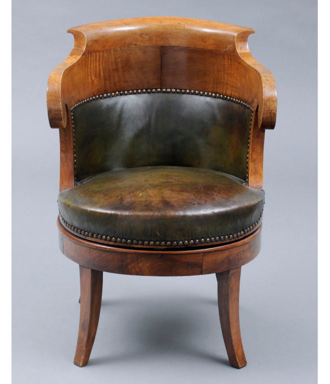 French Restauration walnut swivel fauteuil de bureau, with deep horseshoe-shaped back, scroll arms and saber-shaped legs. The chair is in two sections; the top swivels on the base. Upholstered in old green leather with brass nailheads.