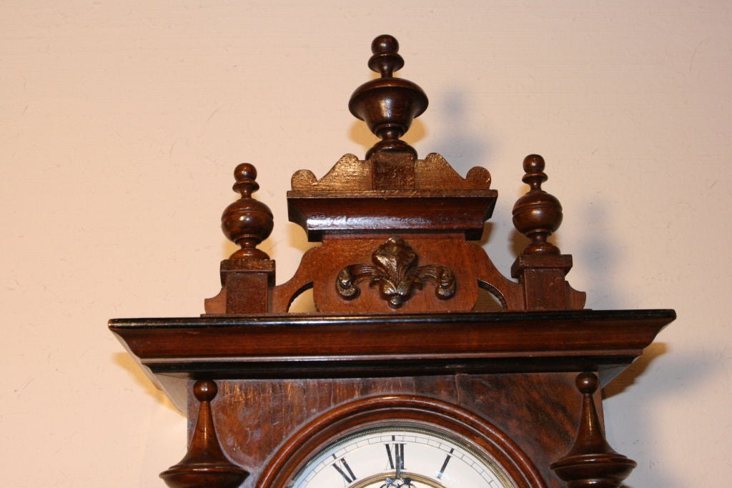 German Miniature 'Berliner' (Free Swinger) wall clock in walnut with the hour and half hour strike.  White enamel face with Roman Numerals.  8 day clock.   Fleur de Lis on pediment<br />
with three finials.<br />
FREE SHIPPING to lower 48 States.