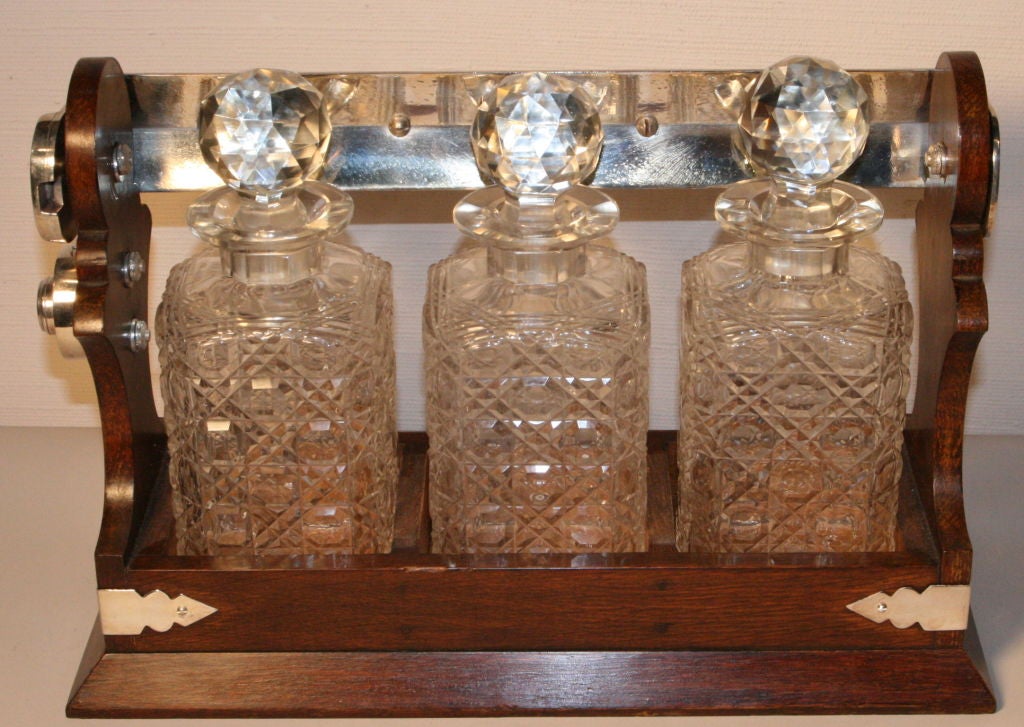 English oak tantalus with 3 liquor decanters all in perfect condition, no chips on stoppers etc. Top handle retracts forwards or backwards to release the decanters and is Silverplate.   Key mechanism is also silverplate which when locked the top