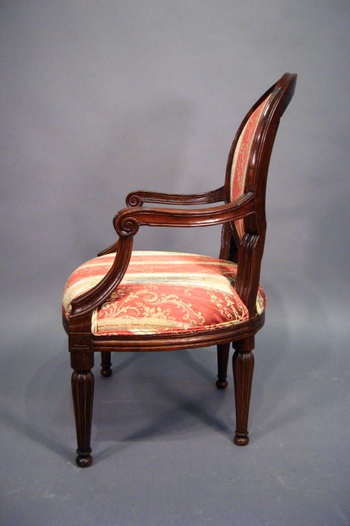 A fine Louis XVI period Fauteuil, with Neoclassical carved designs throughout the exposed Walnut frame. Dating from the fourth quarter of the 1700s, and Italian in origin. 

The oval back with moulded edge and convex profile, supported by a pair