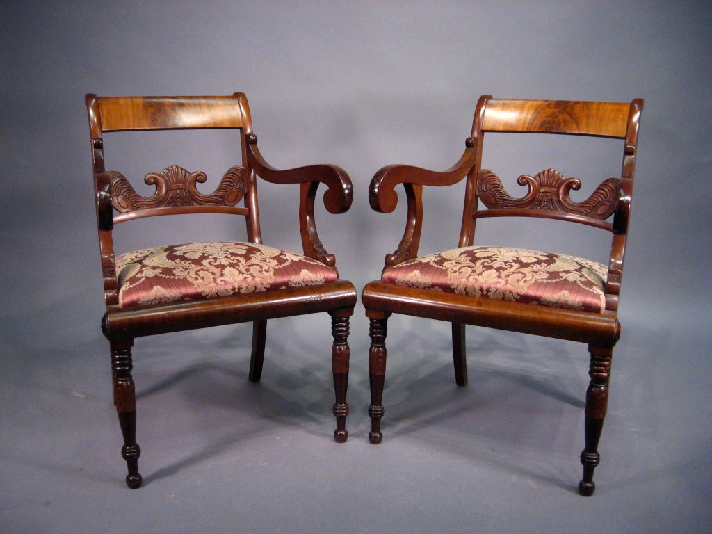 A pair of Austrian armchairs in mahogany with concave crest-rail above a carved back, drop-in seats and cylinder frieze ending in turned front legs and splayed back legs. 

 