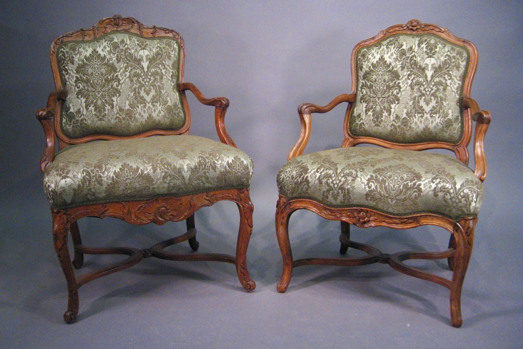 A closely-matched pair of Regence Armchairs, each constructed in elaborately-carved walnut, and dating from the first half of the 1700s. (One c. 1720, the other -shown in Image #6- c. 1740)

The chairs with serpentine-form backs carved with rococo