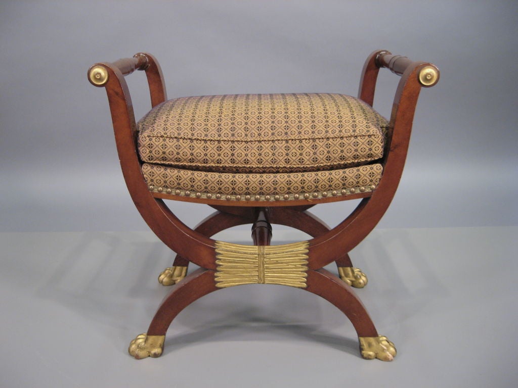 An Empire mahogany and parcel-gilt bench, with X-shaped frame in the neoclassical taste. Dating from the first quarter of the 1800s, and most likely French in origin. Similar stools are illustrated in 