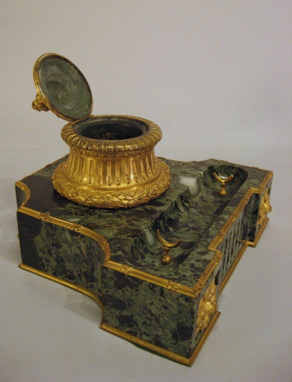 The base is composed of variegated green marble with a pen tray, ormolu trim and patarae motif.  The ormolu well with lid is beautifully decorated with laurel wreath garland surrounding the base flowing up to fluting in the center and a laurel leaf