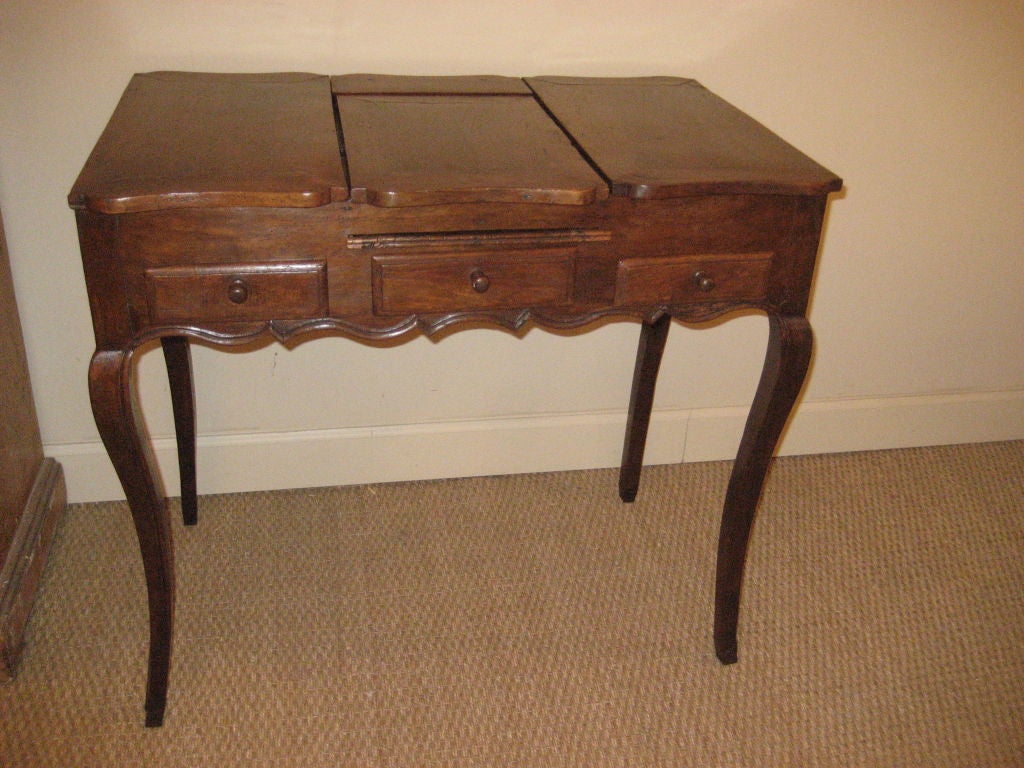An 18th century French Louis XV coiffeuse in walnut, with various compartments and a mirror that folds into the top, a scalloped apron on cabriole legs.
