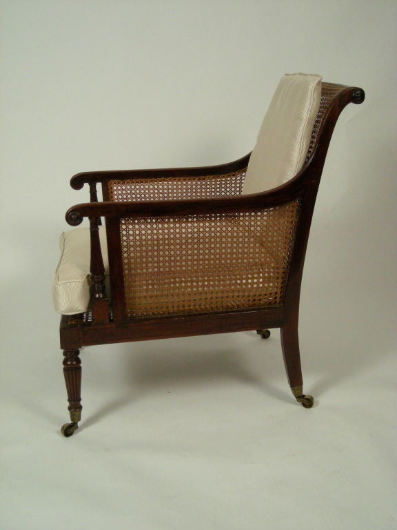 Fine quality English Regency period carved and inlaid mahogany and caned armchair, with original brass caps and castors and with silk upholstered loose back and seat cushion. Generous size, solid and comfortable.