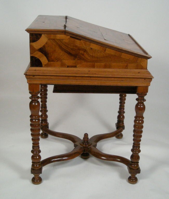 A fine quality Swiss writing desk on stand, the top decorated with geometric marquetry in richly colored and figured European walnut, opening to reveal 3 storage drawers and steel strap hinges, with a single drawer below, the whole resting on  ring