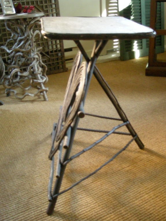 An Adirondack  twig occasional table or plant stand in old black paint the rectangular top over crossed tripod legs, joined by stretchers, the front decorated with large concentric hearts.