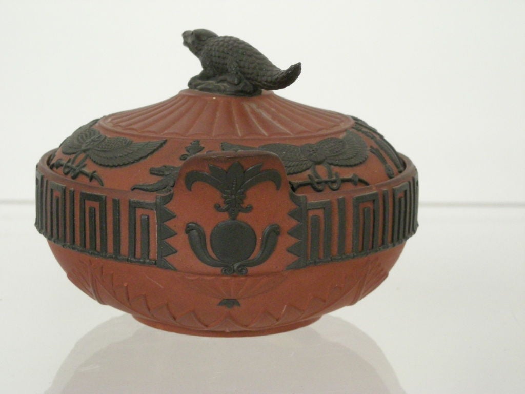 Wegwood 'rosso antico' sugar bowl and cover of circular form with pad handles and applied black basalt hieroglyph relief decoration and crocodile finial, impressed 'Wedgwood' mark.