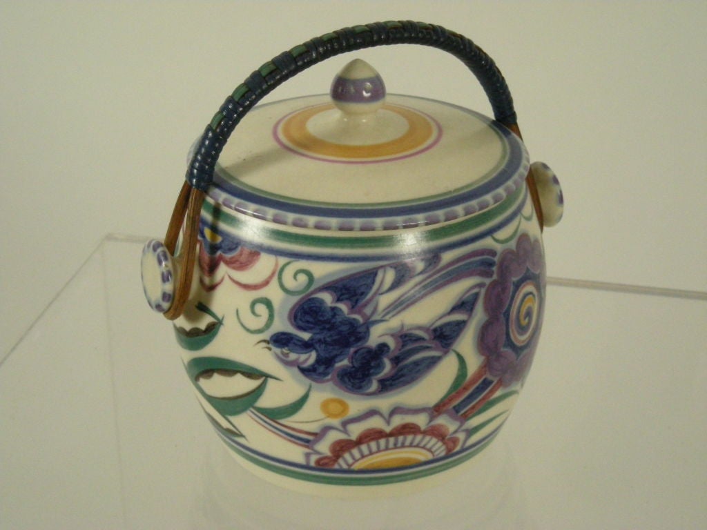 English Art Deco period biscuit jar by Poole Pottery, decorated with stylized flowers, with blue an dgreen rattan handle. Signed.