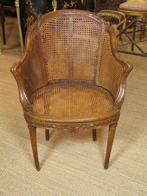 French caned desk chair (fauteuil de bureau) in carved walnut in the  Louis XV/XVI transitional style, with acanthus detailing and fluted legs. Caning is double on the chair sides.