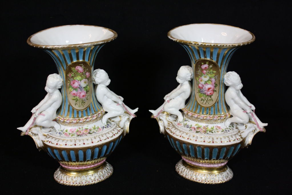 Pair of Paris Porcelain hand painted urns with fluted bodies, putti holding ribbons and gilded details.