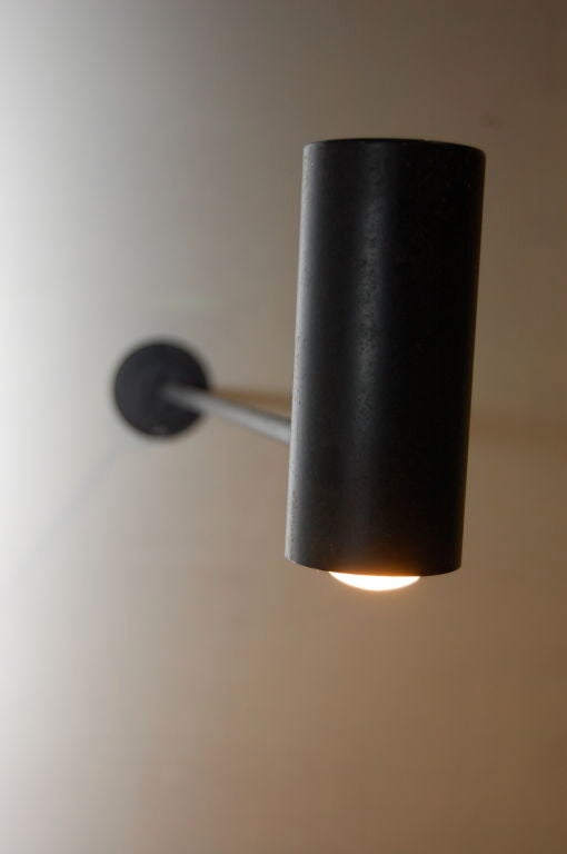 Single arm wall applique in black , fixed circular wall plate , long attached arm and articulating tubular shade with perforated top . Arm extends out a full 24