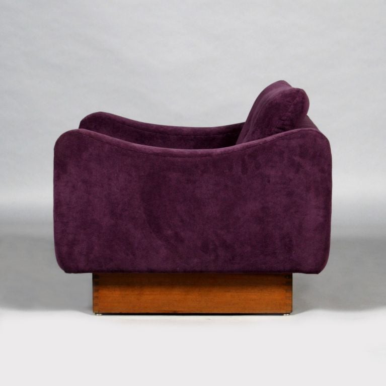 A pair of low easy chairs sitting on a stained oak base with unusual sculpted arms. Although these chairs are low to the ground, they are surprisingly comfortable and perfect for relaxation. They are upholstered in a purple fabric with a heavy pile