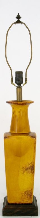 Cette ancienne lampe de table Fredrick Cooper présente un corps en céramique en forme de vase de couleur safran recouvert d'une glaçure rouge incroyablement vive, avec une base en bois sculpté. Vendu sans store.