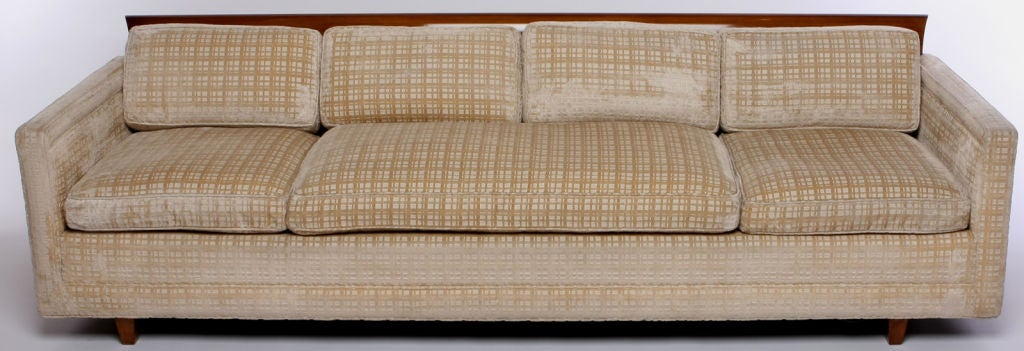 Even arm sofa with architecturally curved walnut wood across the top back. Walnut legs and creamy beige crosshatch textured upholstery over down cushions.