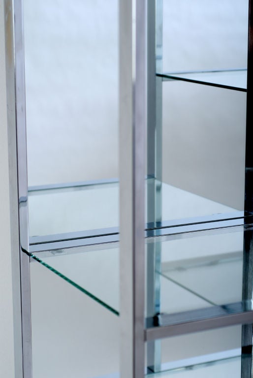 Tall chrome etagere or bookshelf unit with glass shelves and mirrored back in an asymmetrical design.