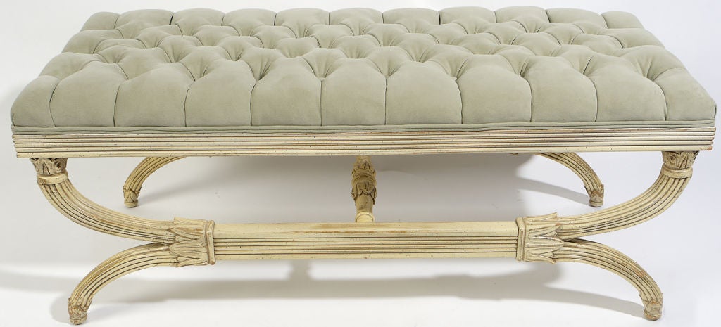Painted in original cream lacquer, the base of this long bench is in a curule form, with reeded legs and a decorative lotus motif.  Newly reupholstered in a button tufted light slate blue ultra suede.