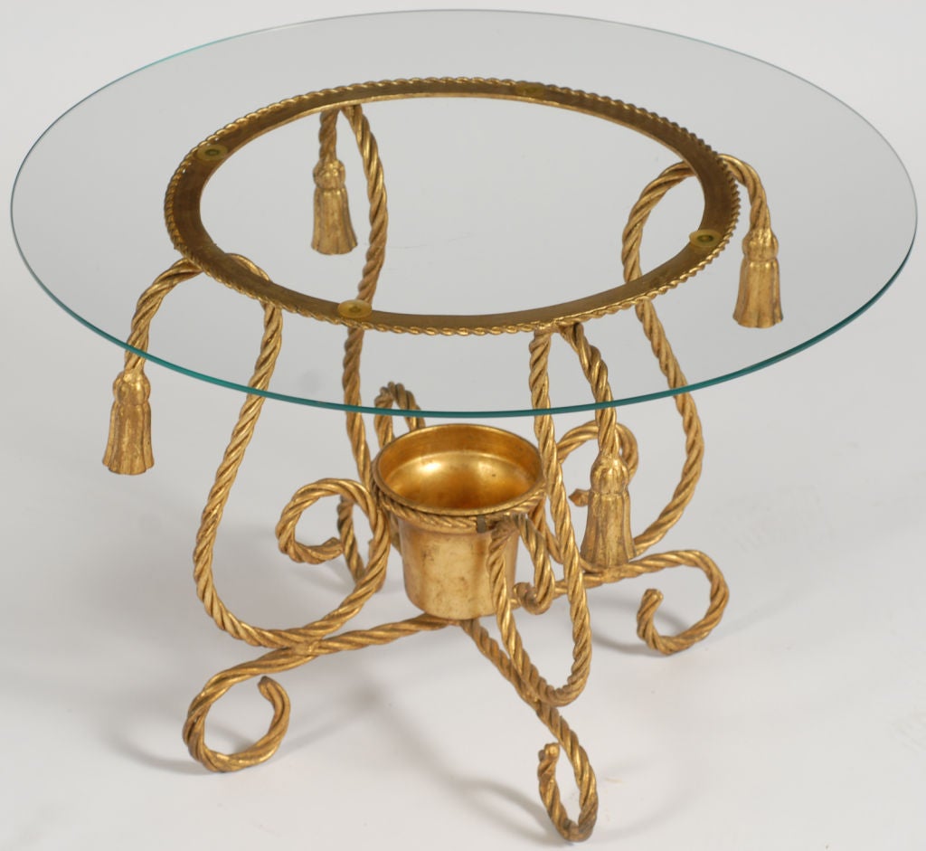 Cette petite table ronde, ou guéridon, a un cadre en fer doré  tressé pour ressembler à une corde.