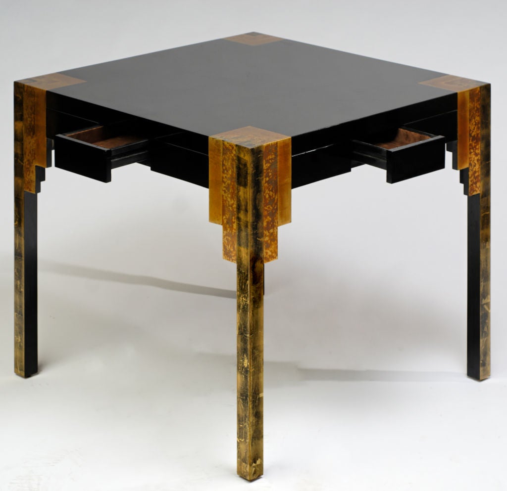 From the 80s art deco revival, this incredible game table has a black lacquer top with three different colors of gold leafing ornamenting the corners and legs.  Each side had a flush mount drawer for game pieces.