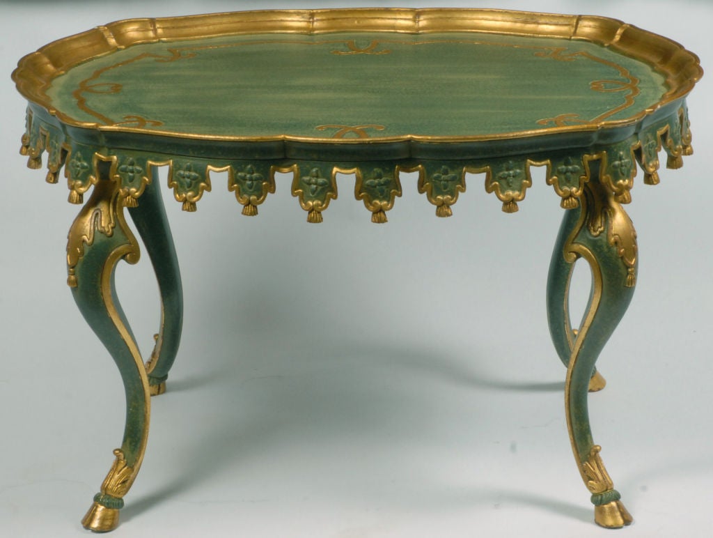 Shaped like a squared-off oval, this table is carved of wood, including tassel ornamentation and hoof feet crested with acanthus leaf trim.  Painted a lovely teal blue-green, with an ivory over glaze, it is accented by gilded trim.  Marked 
