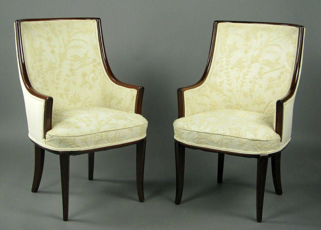 Two lovely armchairs with dark mahogany frames, reminiscent of some Tommi Parzinger designs.  The barrel backs are covered in cream linen, and the interior of the chair is covered in an ivory crewel fabric, with wool yarn on a cream linen ground. 