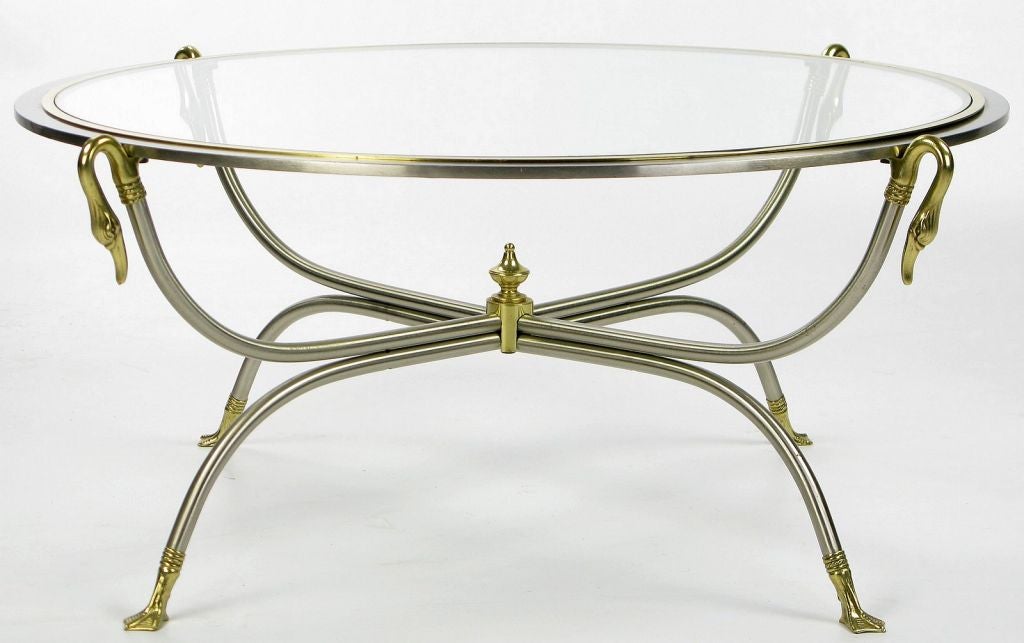 Lovely round coffee table with a double curule frame of nickeled steel and brass.  The clear glass top is surrounded by a nickel and brass frame that is supported by four long brass swans' necks.<br />
<br />
A central brass finial accents the