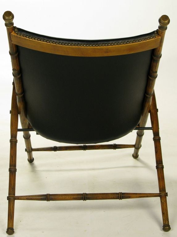 A classic design, with folding wood frame carved to appear as bamboo, brass caps, leather seat and back with brass nailhead trim, and leather arm straps.
