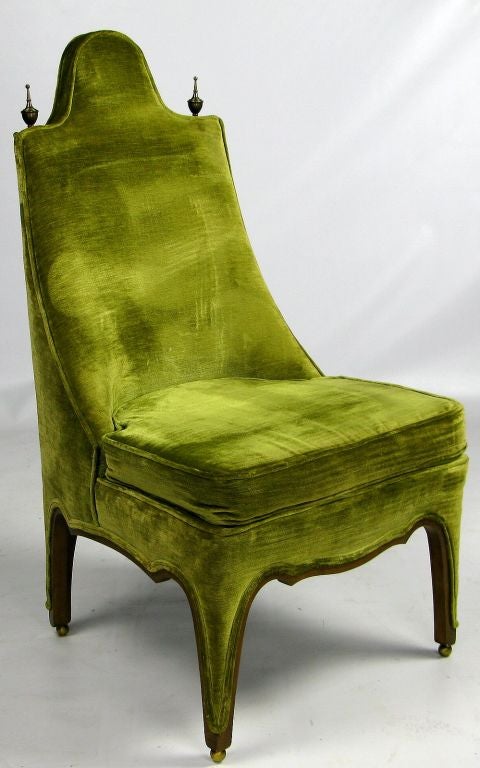 An unusually designed side or slipper chair, with the legs trimmed in walnut wood set atop spherical brass feet.  Green velvet upholstery is accented by tall brass finials on top of each side of the chair back.