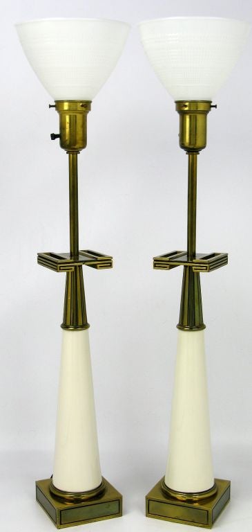 White porcelain conical bodies are set atop brass bases, with brass top incised with vertical radial and Greek key designs.  White milk glass diffusers, sans shades.