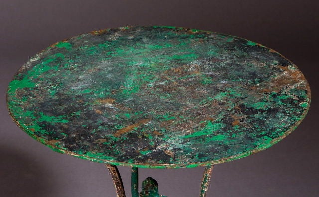 A French, late 19th century, round metal table in old green paint.  Three slender curled legs and acorn details in the center.